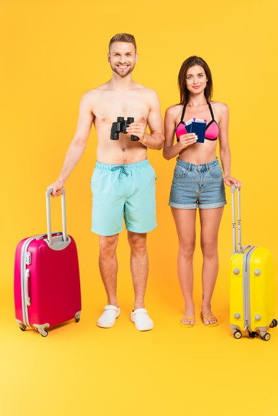 happy couple with binoculars and passports standing near luggage on yellow - Foto, imagen