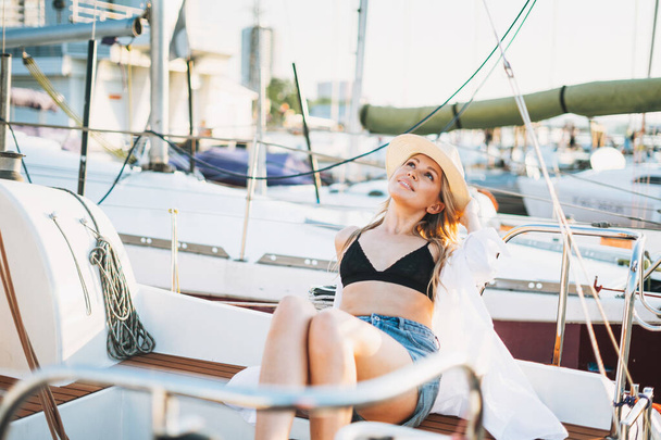 Beautiful sensitive blonde young woman in short and straw hats on the boat at pier - Foto, imagen