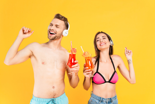 felice uomo e donna in cuffia con cocktail isolati su giallo - Foto, immagini