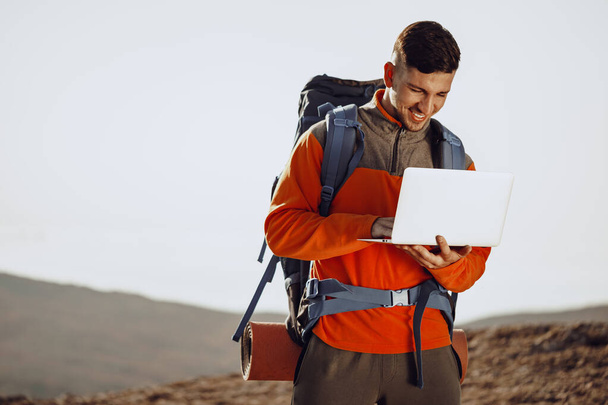 Young man backpacker using his laptop in mountain journey - Foto, Imagen