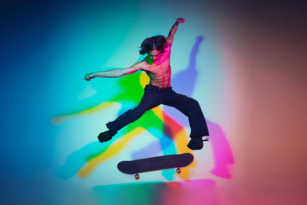 Skateboarder doing a trick isolated on studio background in colorful neon light - Fotoğraf, Görsel