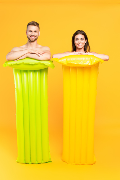 happy couple looking at camera and standing near inflatable mattresses on yellow - Foto, Imagem