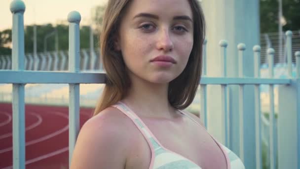 close-up van schattige gezonde jonge vrouw leunend op metalen hek en glimlachen op zoek naar camera, vrije tijd zomerochtend - Video