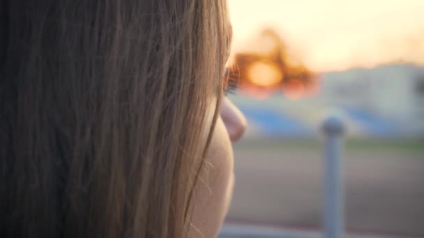 Nahaufnahme Porträt einer hübschen jungen Frau in der Nähe des Sportstadions, die den Sonnenuntergang betrachtet und träumt - Filmmaterial, Video