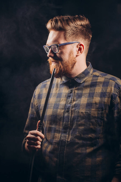 Stylish beard man in glasses and checked shirt smoking hookah at night bar. - 写真・画像
