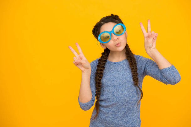 showing piece gesture. kid fashion and beauty. small girl looking cool. childhood happiness. beautiful braided long hair. stylish braids and pigtails. party fun. funny teenage girl in glasses - Foto, Imagen