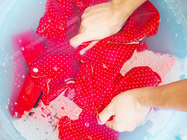 Asiática tailandesa mujer uso manos a lavado y remojar rojo polo camiseta en tela suavizante en azul lavado bañera
. - Foto, Imagen