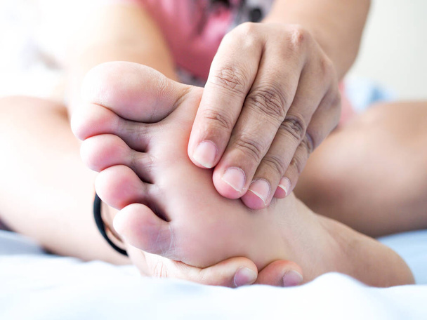 Yatakta oturan Asyalı kadın ayak ağrısı çekiyor. Acıyı hafifletmek için el masajı yap ve ayak kaslarını gevşet. Plantar Fasciitis hastalığı.. - Fotoğraf, Görsel