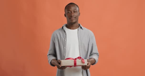 Cheerful black guy offering exclusive gift box to camera - Imágenes, Vídeo
