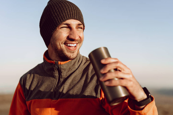 Young man traveler drinking from his thermocup while halt on a hike - Фото, зображення