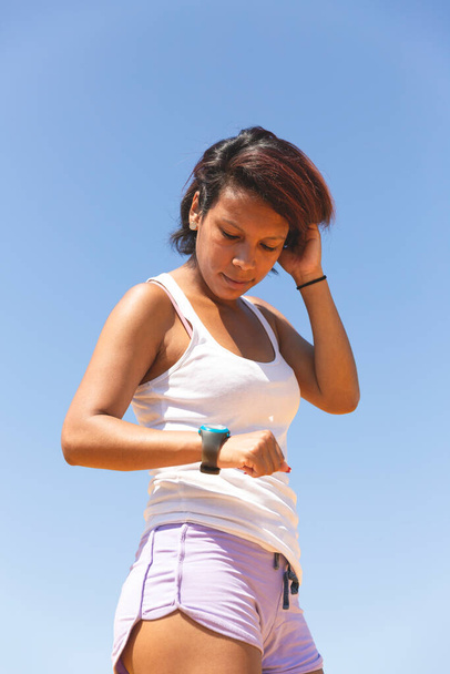Retrato de una deportista mirando un cronómetro. Ella está al aire libre y lleva una camiseta y pantalones cortos. Espacio para texto
. - Foto, Imagen