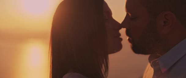 Close up of a young couple looking at each other with love at sunset, with beautiful sun flare behind them. Slow motion.   - Footage, Video