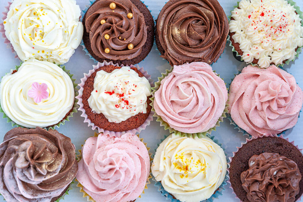 Zelfgebakken cupcakes prachtig versierd met boterroom bovenop netjes geplaatst in kartonnen transportcontainer. - Foto, afbeelding
