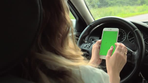 Τα χέρια των γυναικών κρατούν ένα τηλέφωνο με μια πράσινη οθόνη με τα χέρια τους στο τιμόνι του αυτοκινήτου. Το κορίτσι οδηγός κάθεται στο τιμόνι κρατώντας ένα τηλέφωνο με ένα κλειδί chroma στα χέρια της - Πλάνα, βίντεο