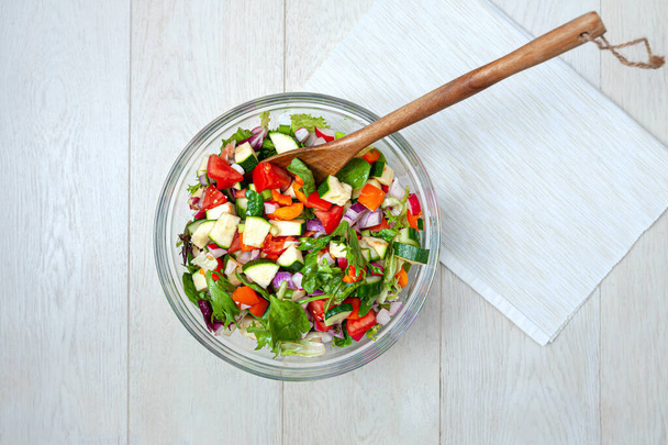 Fresh and healthy vegetables for salad in a glass bowl placed on white wooden surface. - Photo, Image