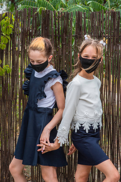 İki kız öğrenci maske takıyor ve covid-19 salgını sırasında okula dönüyorlar. Koruyucu maskeler takan iki liseli kız. Virüs, bakteri, okul, koruma. Okul üniformalı genç kızlar. - Fotoğraf, Görsel