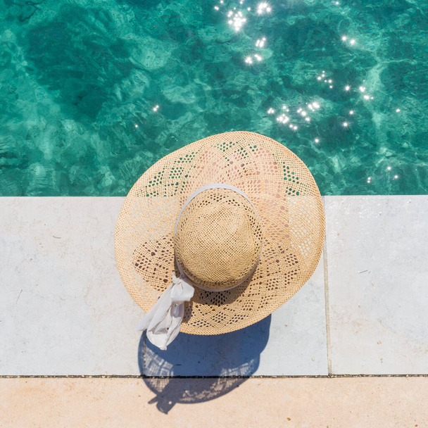 Büyük yaz şapkası takan kadın turkuaz açık denizde iskelede dinleniyor.. - Fotoğraf, Görsel
