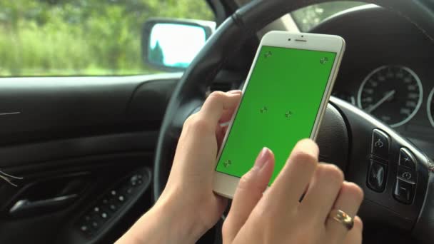 Les mains des femmes tiennent un téléphone avec un écran vert avec leurs mains sur le volant de la voiture. La conductrice est assise au volant tenant un téléphone avec une clé chromatique dans ses mains - Séquence, vidéo