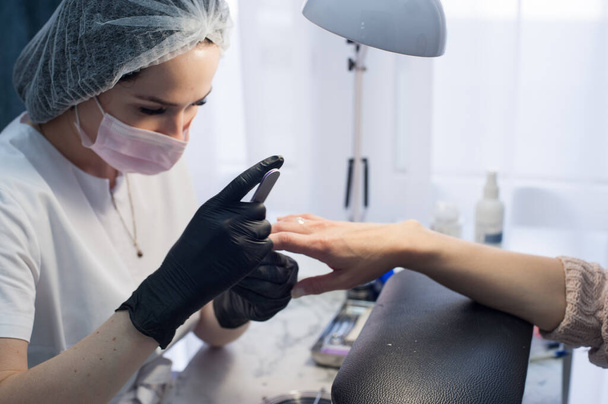 Manicure master in a mask and gloves in the salon. Care at a social distance. Security - Photo, Image