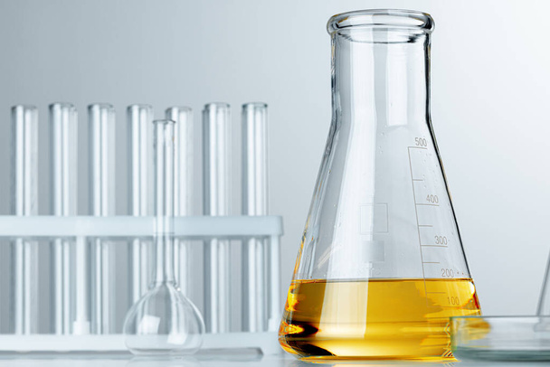Laboratory glassware with yellow oily liquid on grey background - Фото, изображение