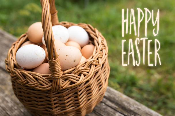 basket with white and brown bio eggs, green meadow in the background, text happy easter - Foto, Imagem