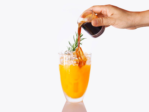 Κάντε το καλοκαίρι ποτό με το pour καφέ αναμειγνύεται σε ποτήρι χυμό πορτοκαλιού πάγο δροσερό απομονωμένο σε λευκό φόντο. - Φωτογραφία, εικόνα