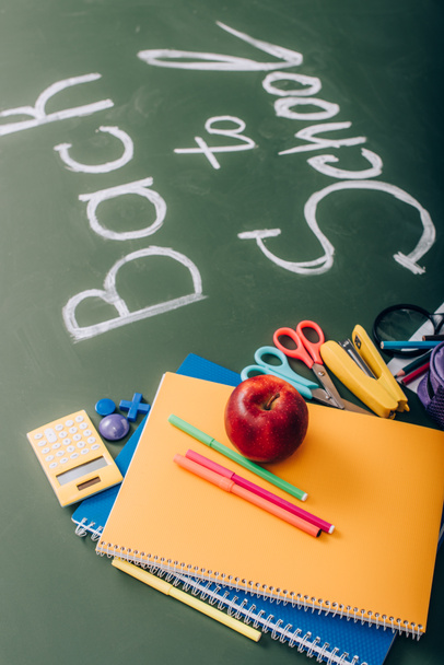 selective focus of school supplies and fresh apple near back to school text on green chalkboard - Фото, изображение