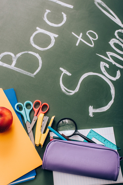 selective focus of back to school lettering near school stationery and fresh apple on green chalkboard - Фото, изображение