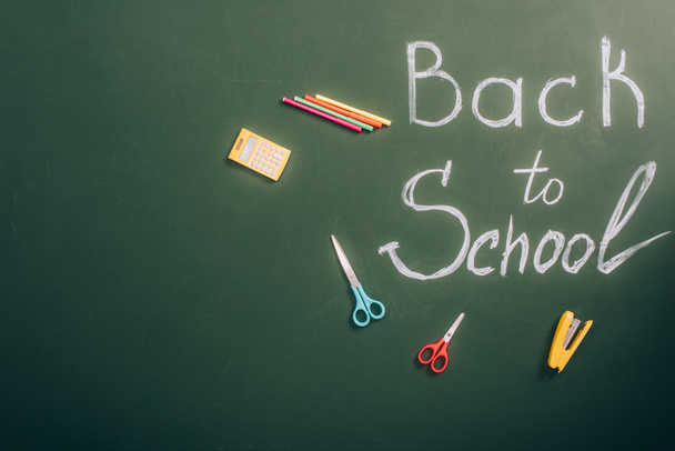 top view of back to school inscription near school stationery on green chalkboard with copy space - Foto, Imagem