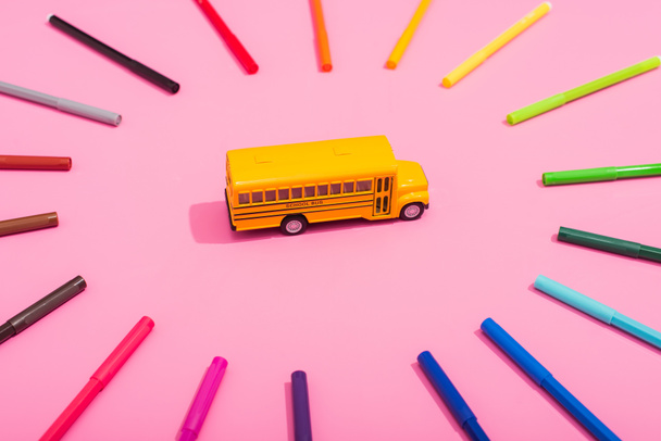 high angle view of school bus model in frame of multicolored felt pens on pink  - Photo, Image