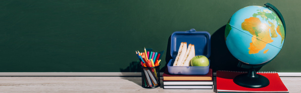 horizontal image of globe near lunch box on books and pen holder near green chalkboard - Photo, Image