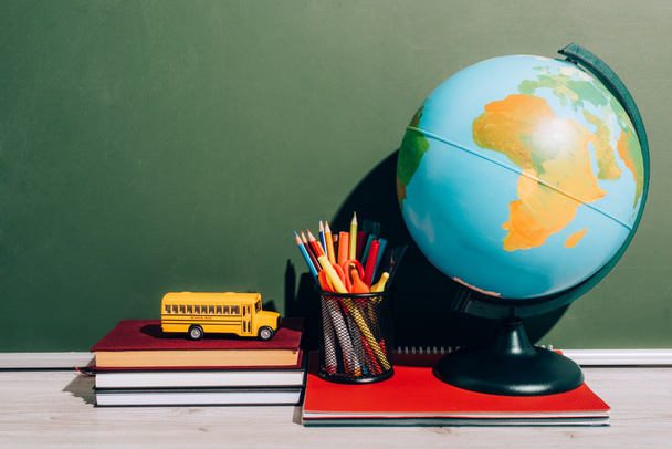 globe and pen holder on notebook near school bus model on books near green chalkboard - Photo, Image