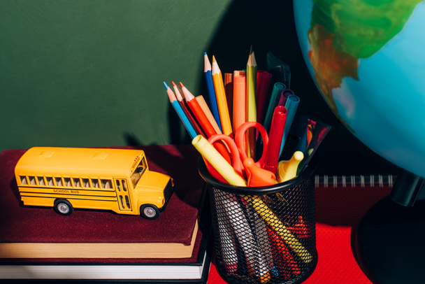 modelo de autobús escolar en libros, porta bolígrafos con papelería y globo cerca de pizarra verde
 - Foto, Imagen