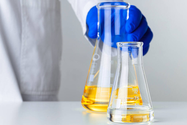 Scientist or doctor in blue gloves pouring some yellow liquid into a flask - Fotoğraf, Görsel