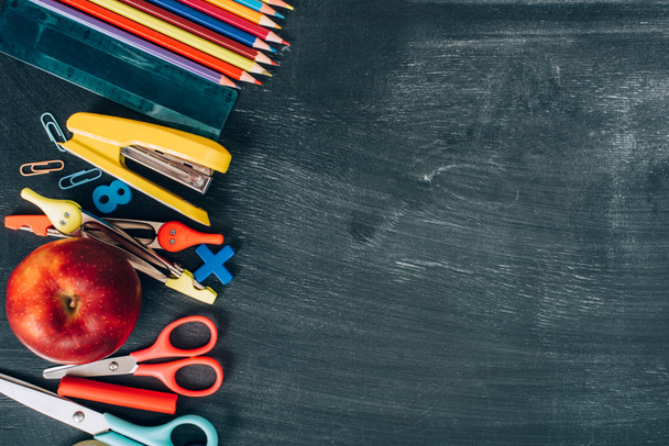 top view of school supplies and ripe apple on black chalkboard with copy space - 写真・画像