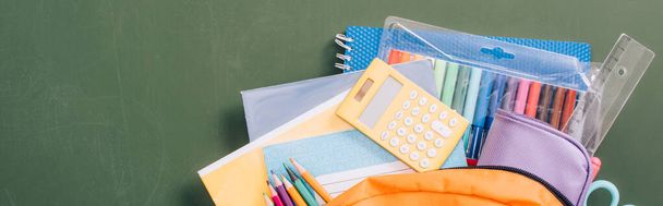 top view of backpack full of school stationery on green chalkboard, horizontal image - Photo, Image