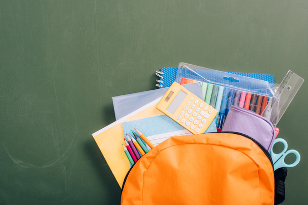top view sárga hátizsák tele iskolai kellékek zöld táblán - Fotó, kép