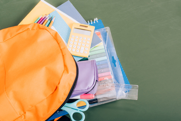 high angle view of yellow backpack with school supplies on green chalkboard - 写真・画像