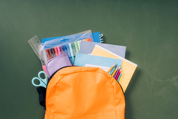 vista superior de la mochila escolar con papelería en pizarra verde
 - Foto, Imagen