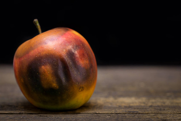 rotten apple on a wooden table, looks like wearing a mask - Fotó, kép
