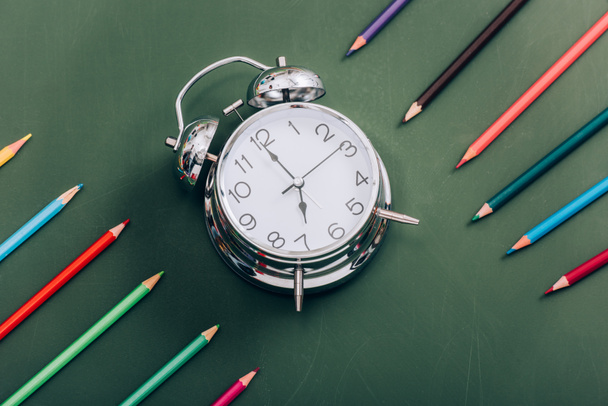 vista de ángulo alto del reloj despertador vintage cerca de lápices de color en pizarra verde
 - Foto, Imagen