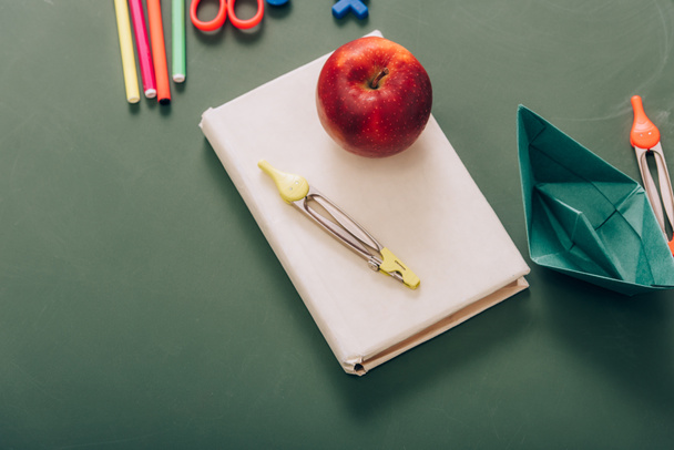top view of tasty apple and compass divider on book near school supplies on green chalkboard - 写真・画像