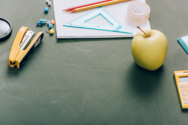 rijpe appel, kopieerboek en schoolbenodigdheden op groen schoolbord - Foto, afbeelding