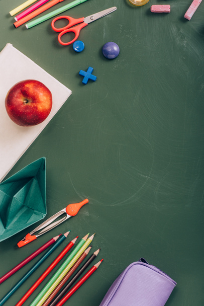 top view of ripe apple on book, paper boat and school supplies on green chalkboard - Photo, Image