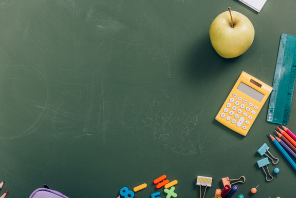 top view of ripe apple and calculator near school supplies on green chalkboard - 写真・画像