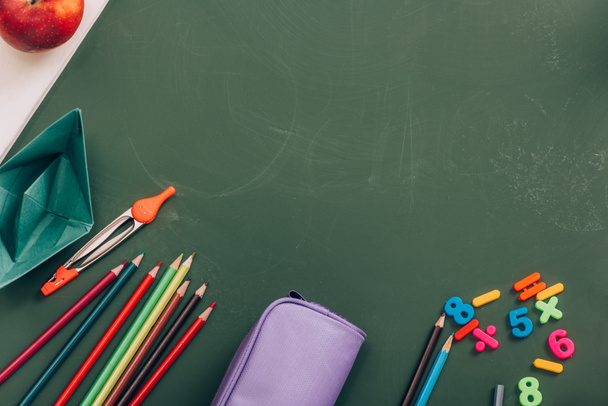 top view of school stationery, paper boat and whole apple on green chalkboard - 写真・画像