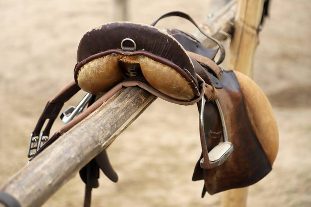 Sportovní kůň zblízka a staré kožené sedlo připravené na drezurní trénink. Jezdecké sportovní zázemí - Fotografie, Obrázek