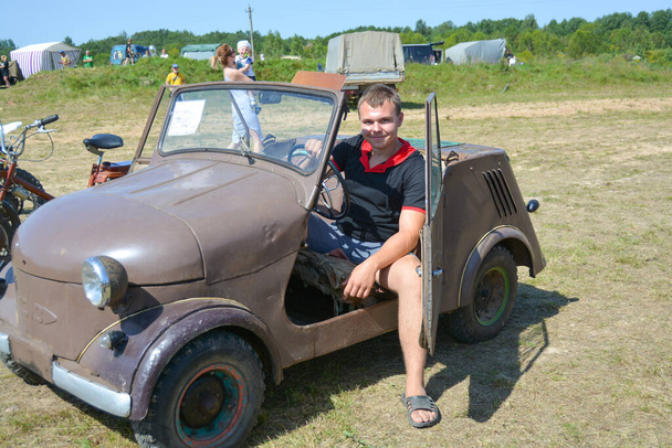 A teenager sits in an old restored car at an exhibition of vintage cars that took place in the summer of 2019 in the city of Kuvshinovo, Tver region - Photo, Image