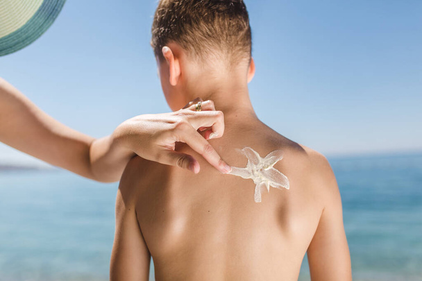 Máma pomocí opalovací krém chránit syna před sluncem během letní dovolené na moři. - Fotografie, Obrázek