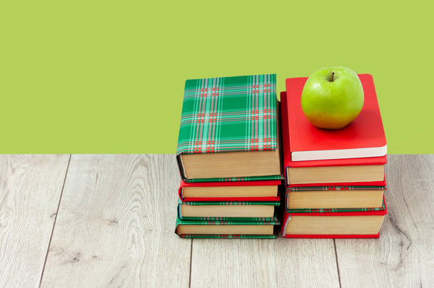 Back to school, pile of books in colorful covers and green apple on wooden table with lime mint green background. Distance home education. Quarantine concept of stay home - Fotografie, Obrázek